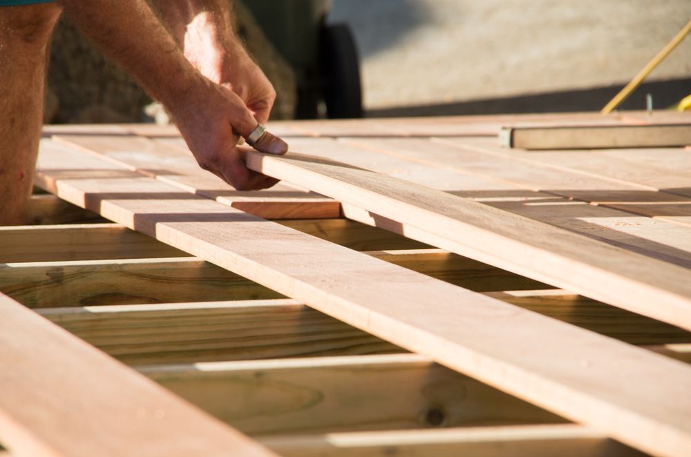 Hands placing a wooden plank on a deck frame during construction — FNQ Footprints Plumbing In Whitfield, QLD