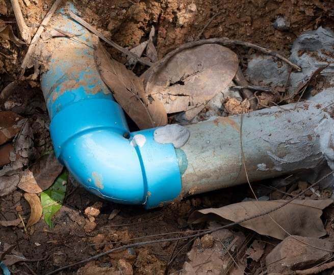 Blue Pvc Pipe Elbow Joined to A White Pipe Buried in Dirt — FNQ Footprints Plumbing In Whitfield, QLD