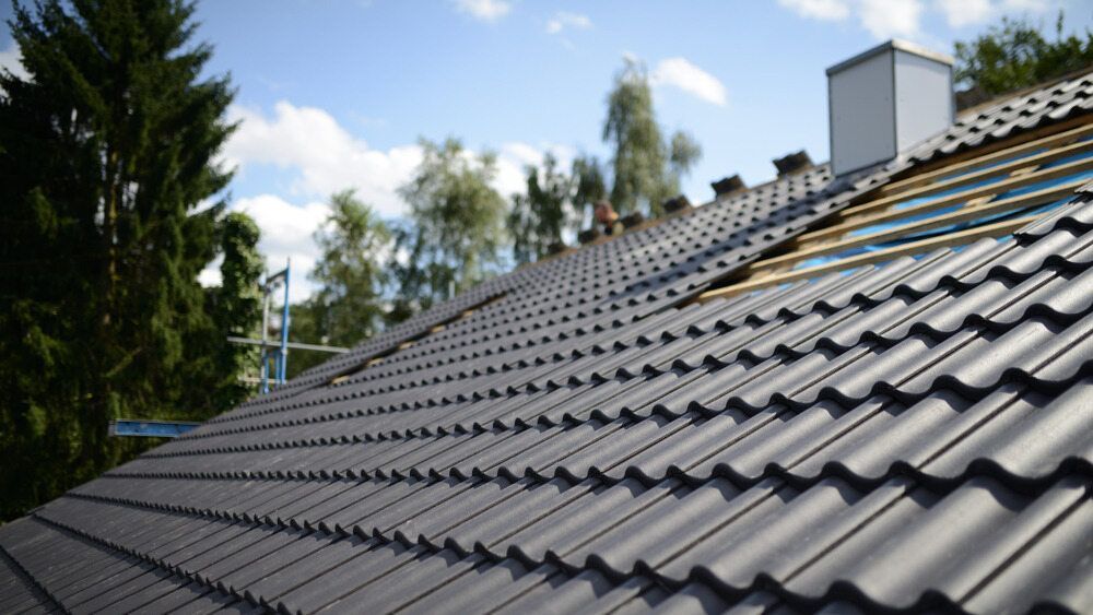 Dark Gray Tiled Roof with A Partially Exposed Section, Trees, and A Chimney Against a Blue Sky — FNQ Footprints Plumbing In Whitfield, QLD