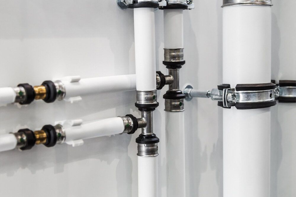 White Pipes and Fittings Attached to A White Wall with Metal Clamps — FNQ Footprints Plumbing In Whitfield, QLD
