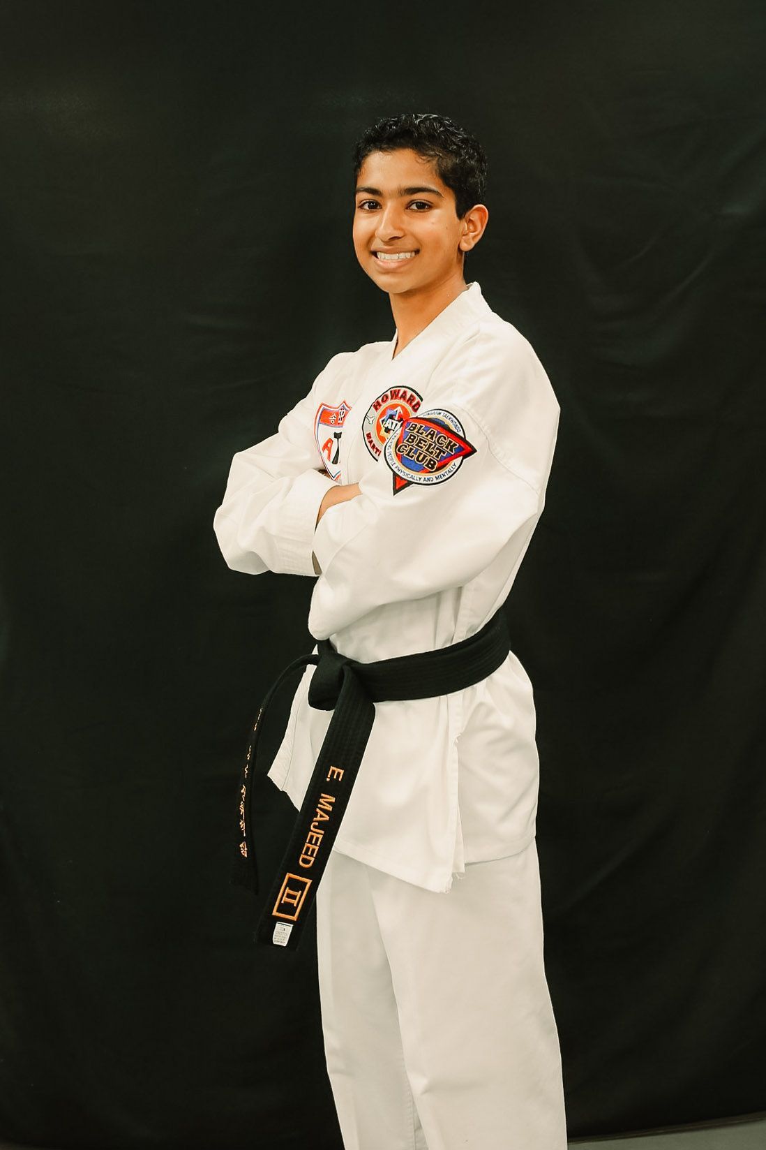 A young boy in a karate uniform is standing with his arms crossed.
