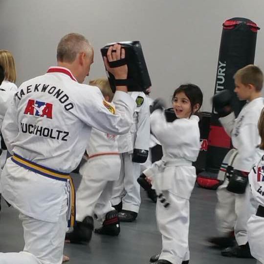 A man in a taekwondo uniform is teaching a group of children