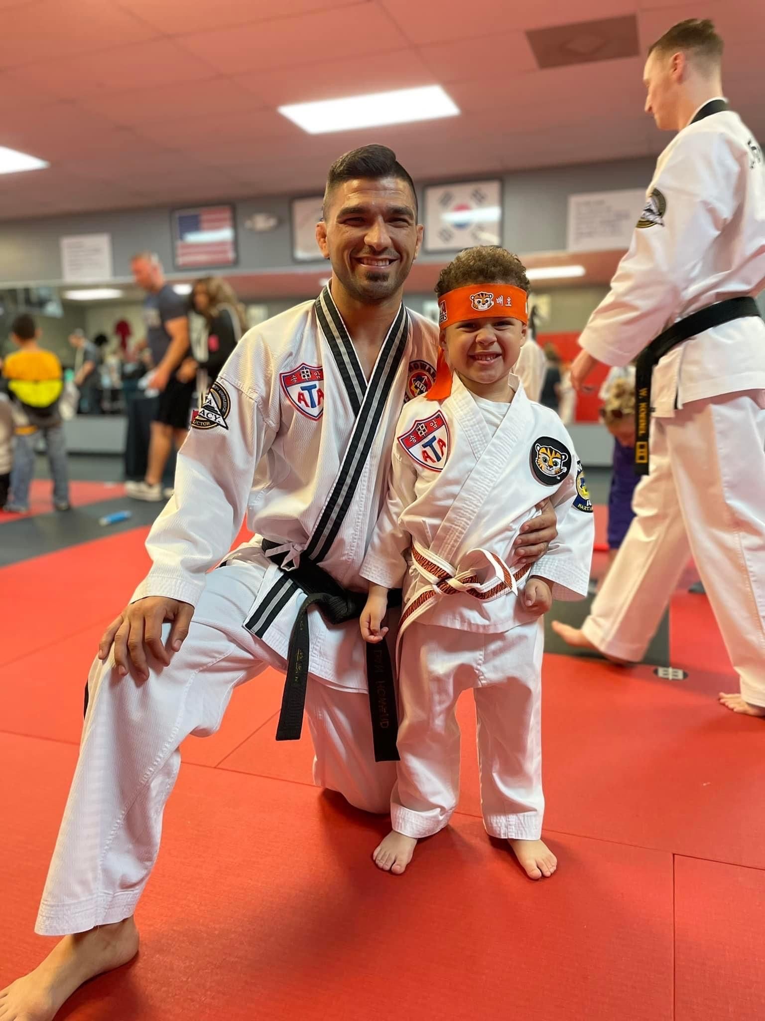 A man and a little boy are posing for a picture in a martial arts gym.