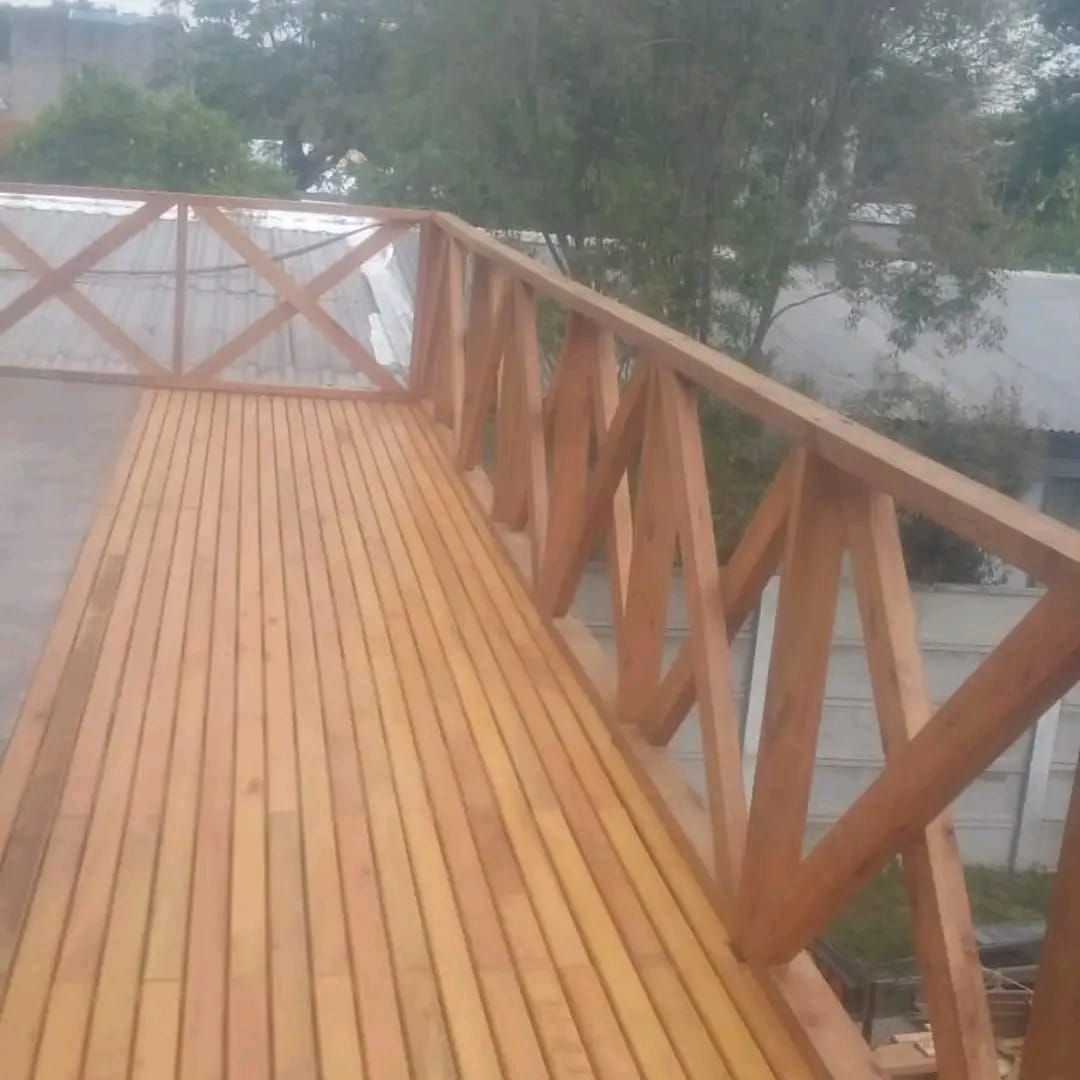 Deck de madera con barandilla y suelo de tarima marrón, exterior, cielo nublado.