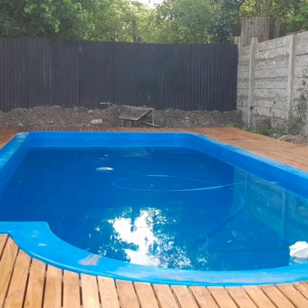 Piscina rectangular azul con cubierta de madera, valla oscura y pared de hormigón al fondo.