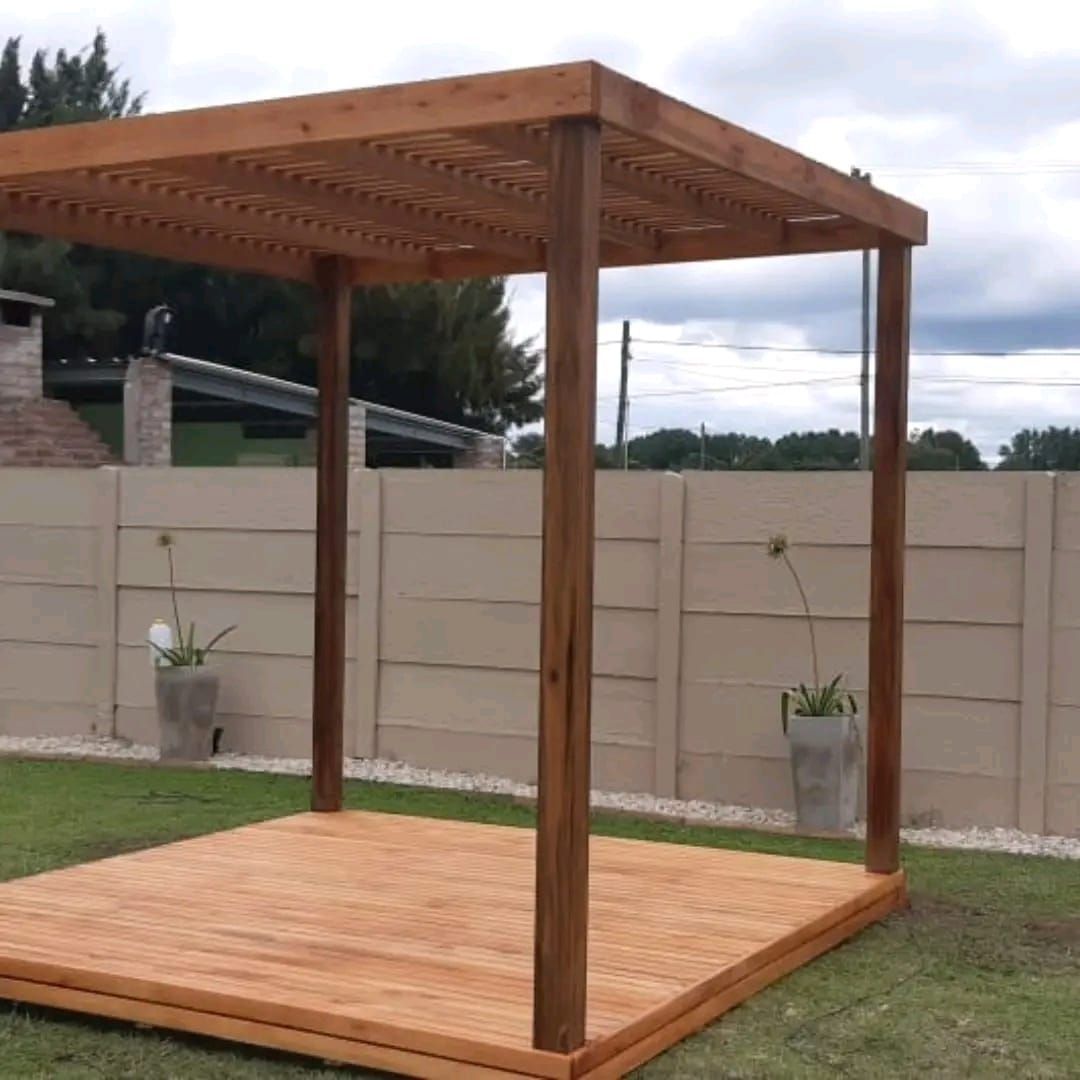 Pérgola de madera con deck en patio trasero, de color marrón con valla de color claro y césped verde.