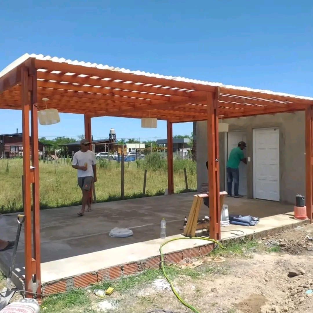 Pérgola de madera con gente trabajando cerca de un edificio en un día soleado.
