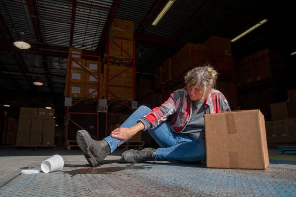A woman is sitting on the floor in a warehouse after a slip and fall.