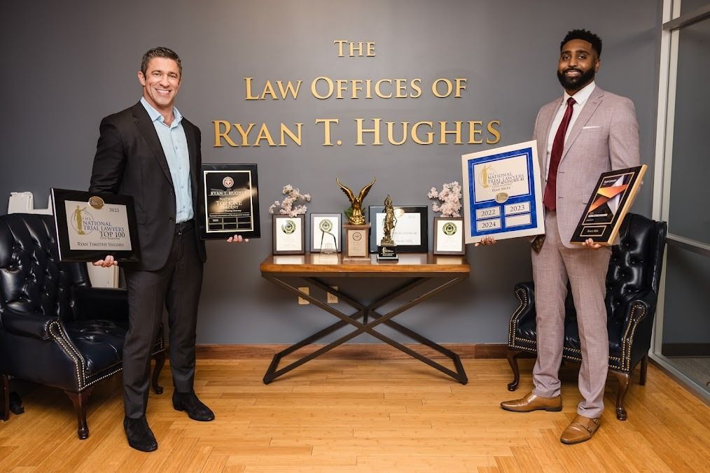 Two men are standing in front of a wall that says the law offices of ryan t. hughes.