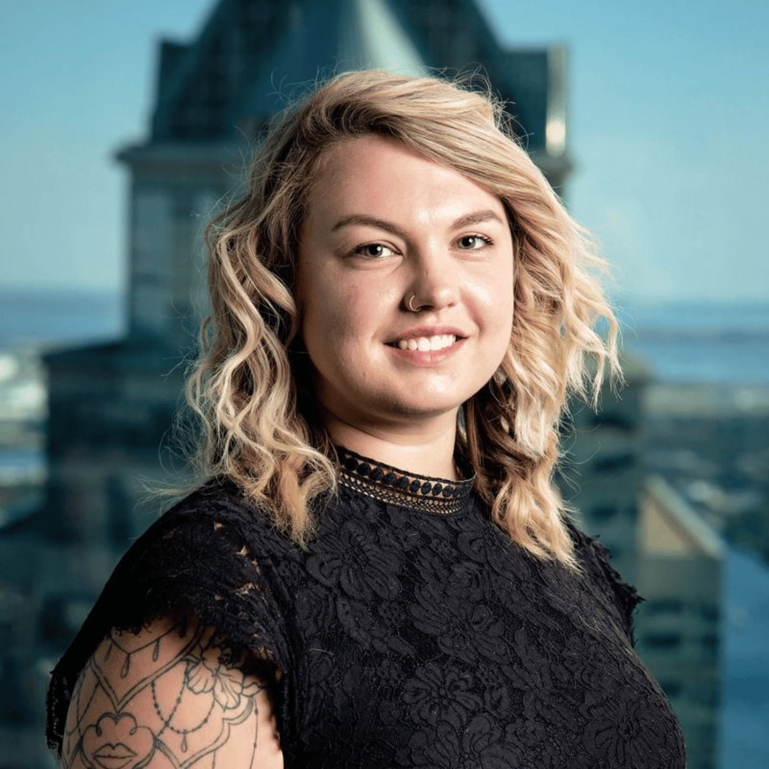 The woman is wearing a black lace top and has a tattoo on her arm.