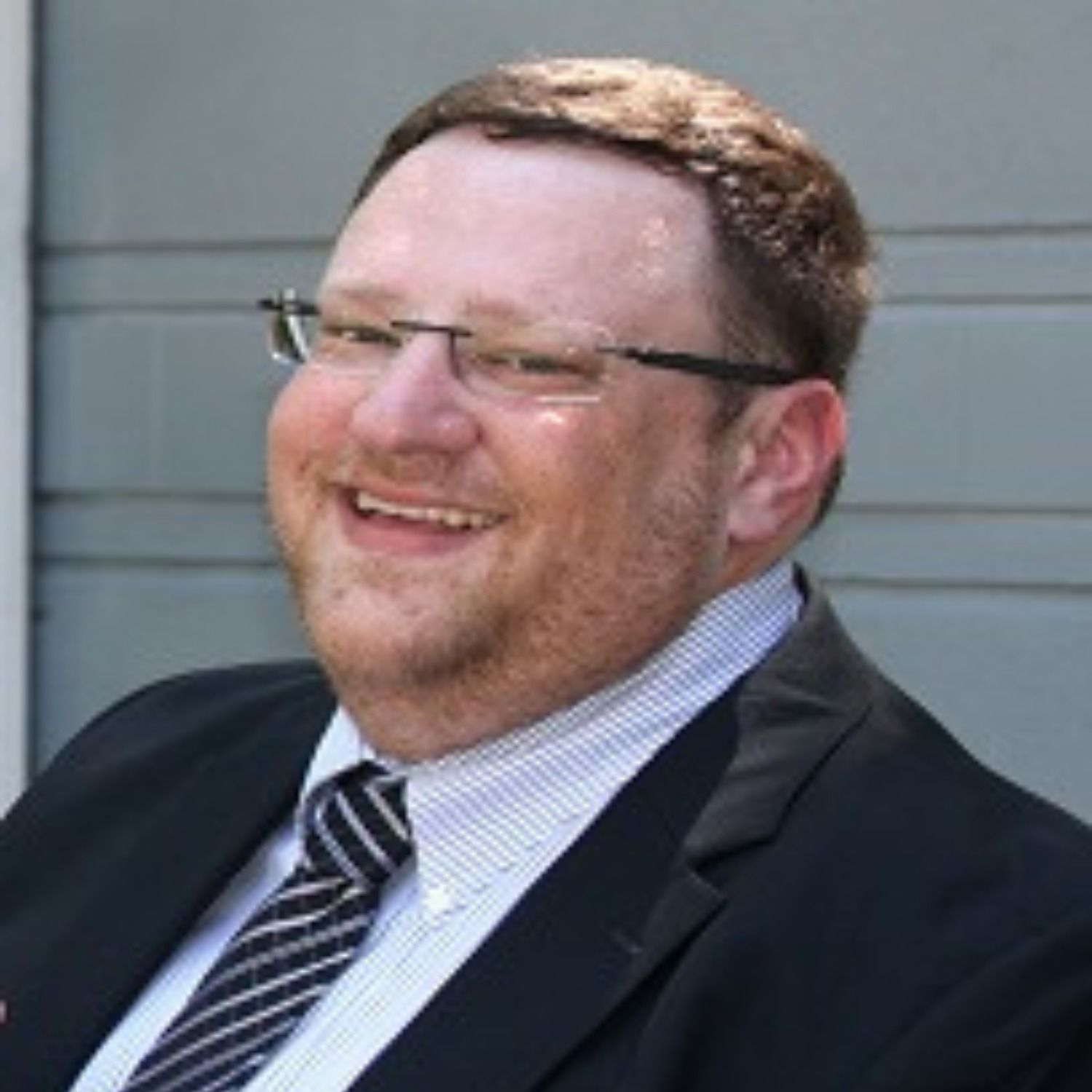 A man in a suit and tie is smiling and wearing glasses