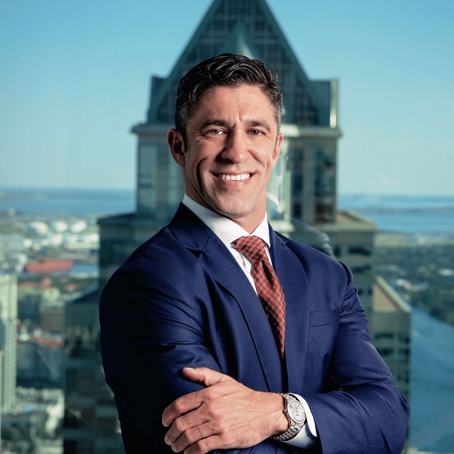 A man in a suit and tie is standing with his arms crossed in front of a building.