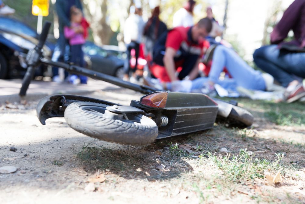 A person is sitting on the ground with a scooter on the ground.