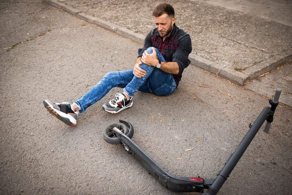A man is sitting on the ground next to an electric scooter.