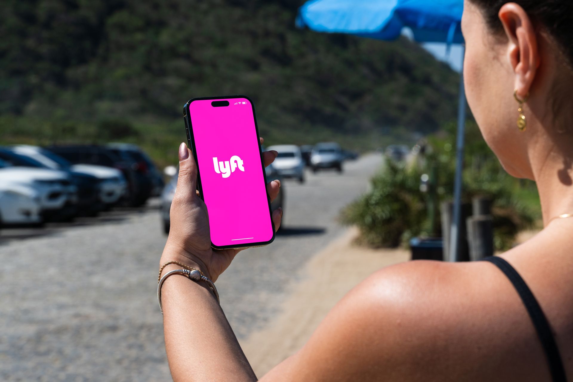 Woman holding a phone with the Lyft app open, with a parking lot and cars in the background.