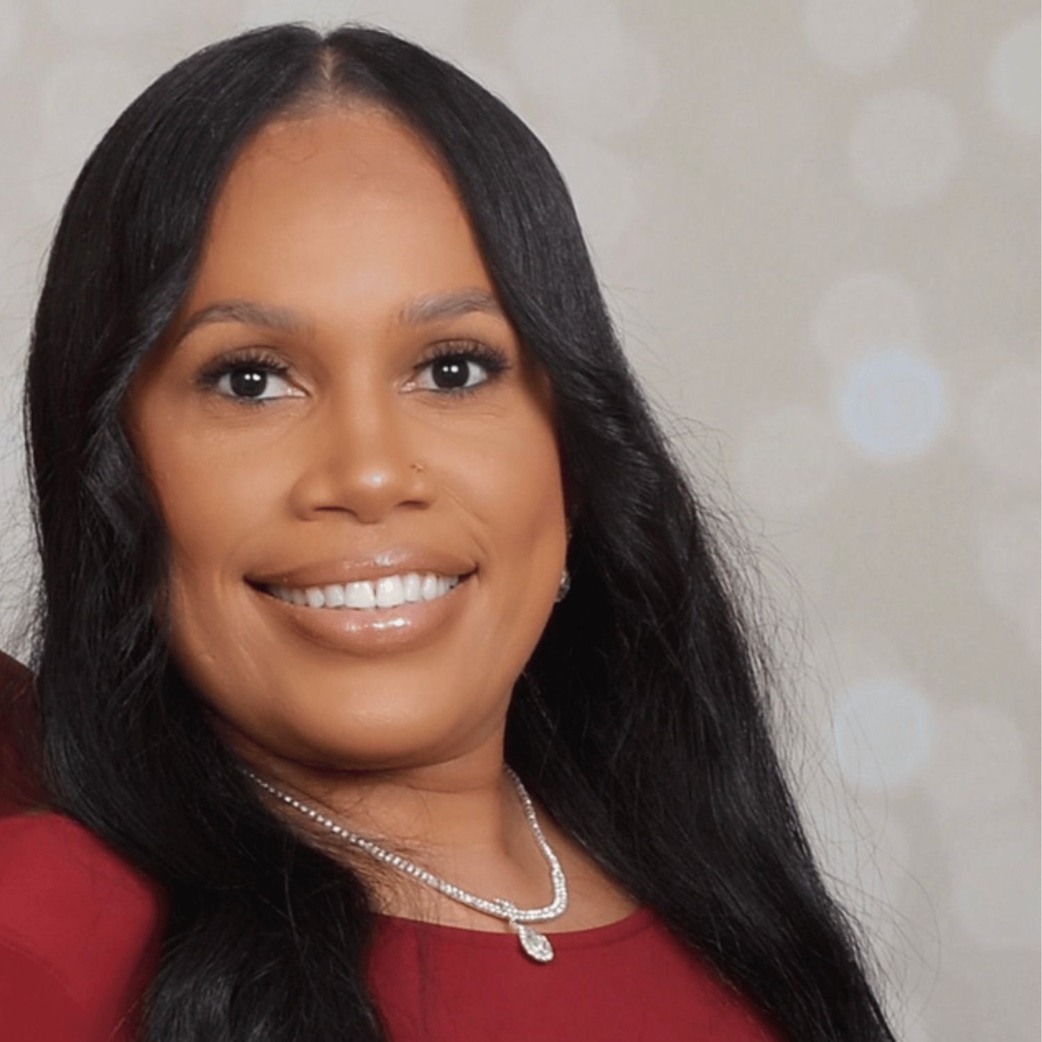 A woman with long black hair and a necklace is smiling for the camera.