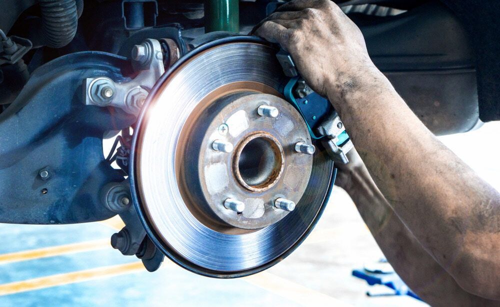 A Man Is Fixing A Brake Disc On A Car — Figtree Brake & Clutch Services in Unanderra, NSW