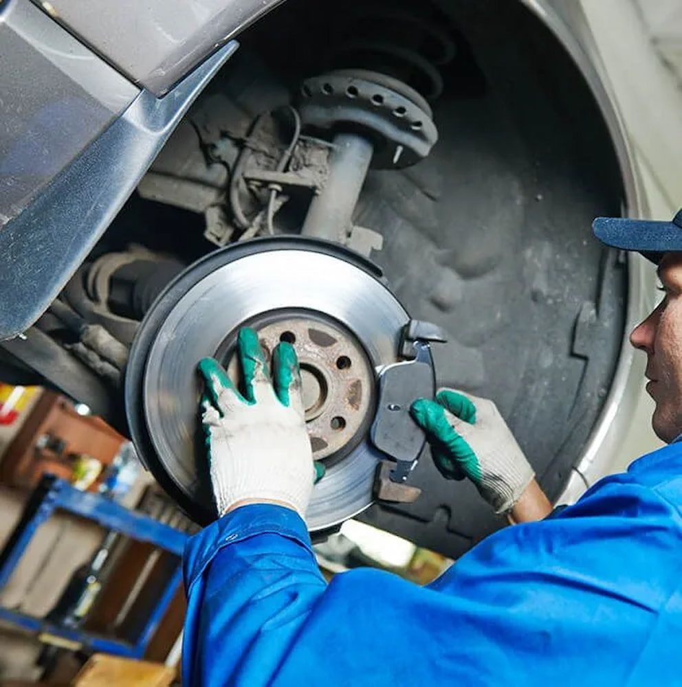 A Man Wearing Green Gloves Is Working On The Brake Pads Of A Car — Figtree Brake & Clutch Services in Figtree, NSW