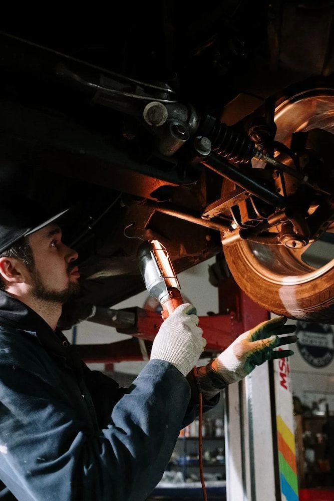 A Man Is Working Under A Car With A Flashlight — Figtree Brake & Clutch Services in Figtree, NSW