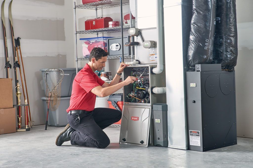 A man in a red shirt is working on a furnace in a garage.