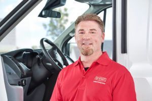 A man in a red shirt is standing in front of a white van.