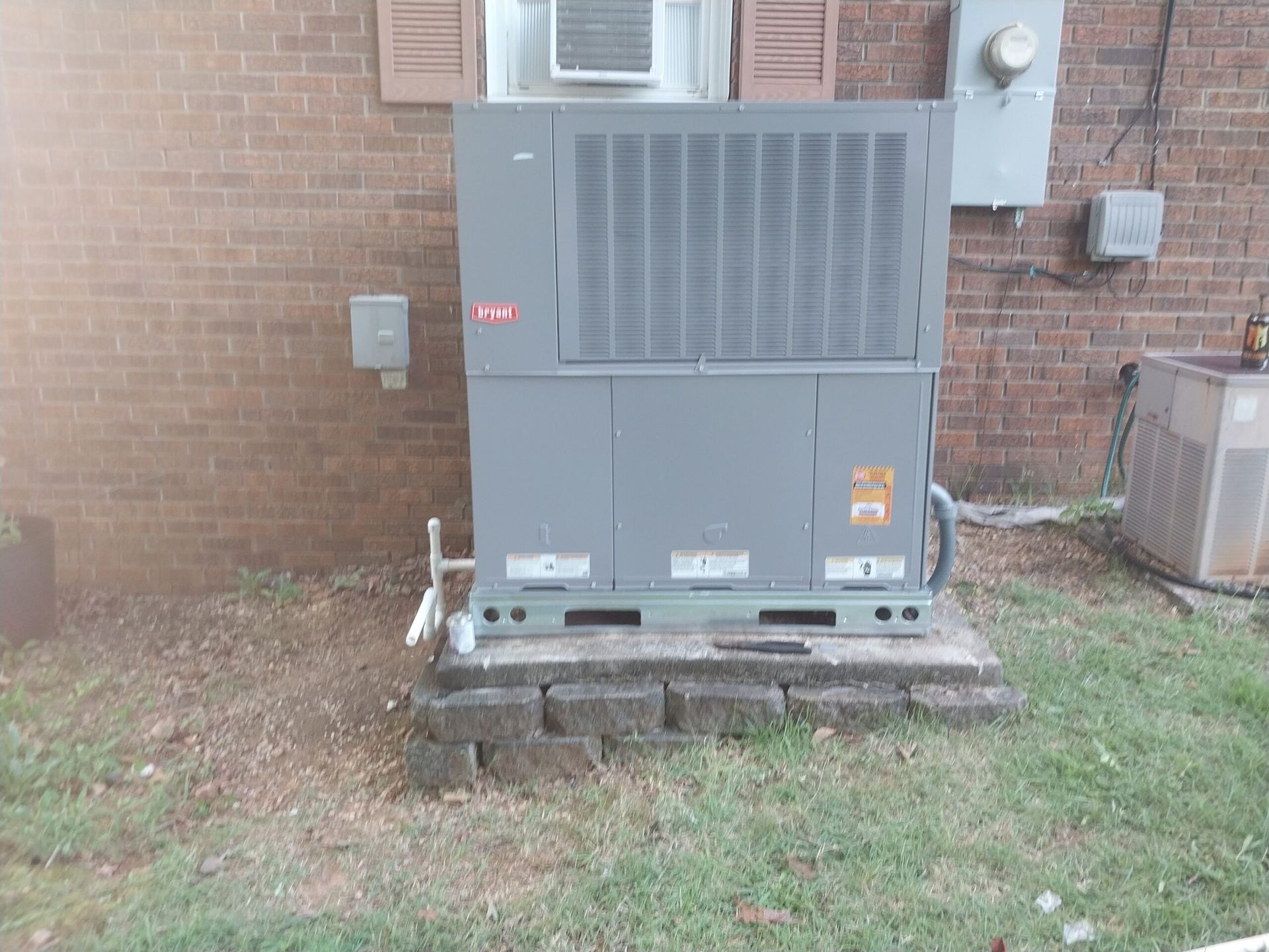 A large air conditioner is sitting outside of a brick building.