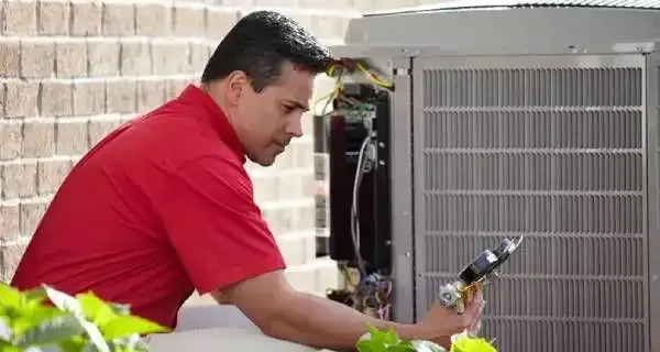 A man in a red shirt is working on an air conditioner.