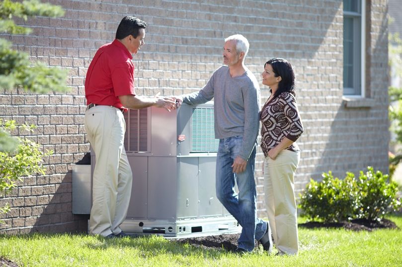 A man in a red shirt is talking to two people in front of a house.