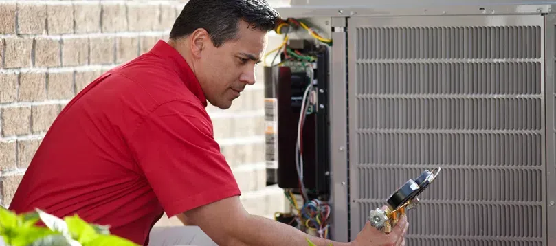 A man in a red shirt is working on an air conditioner.