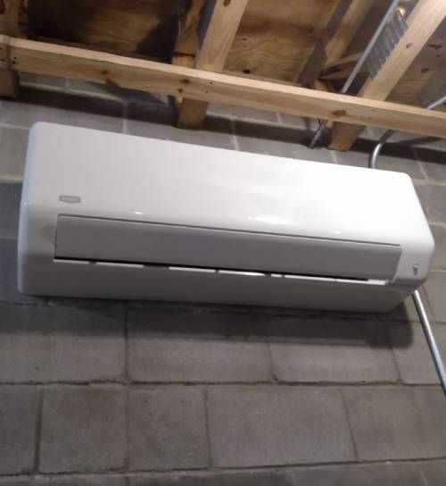 A white air conditioner is sitting on a brick floor