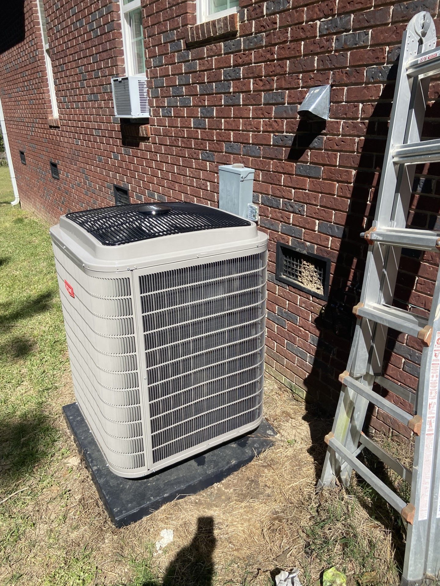 A large air conditioner is sitting on the side of a brick building next to a ladder.