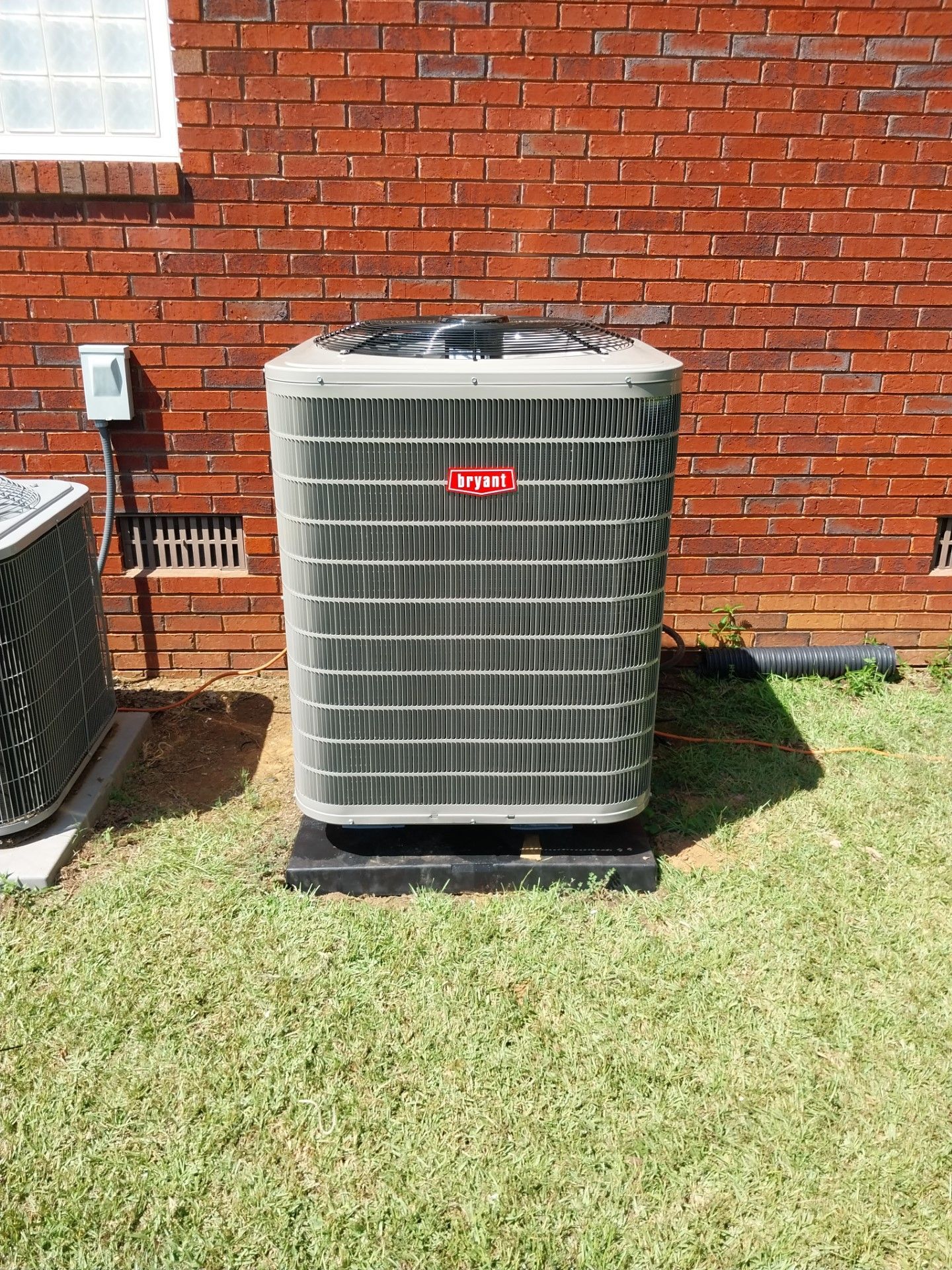 A large air conditioner is sitting in the grass in front of a brick building.
