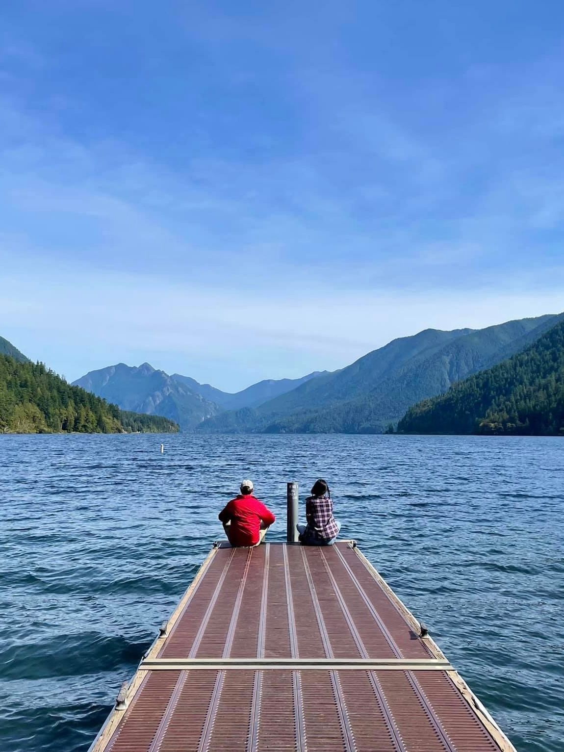 John and Becca are sitting on a dock overlooking Lake Crescent in Olympic National Park.