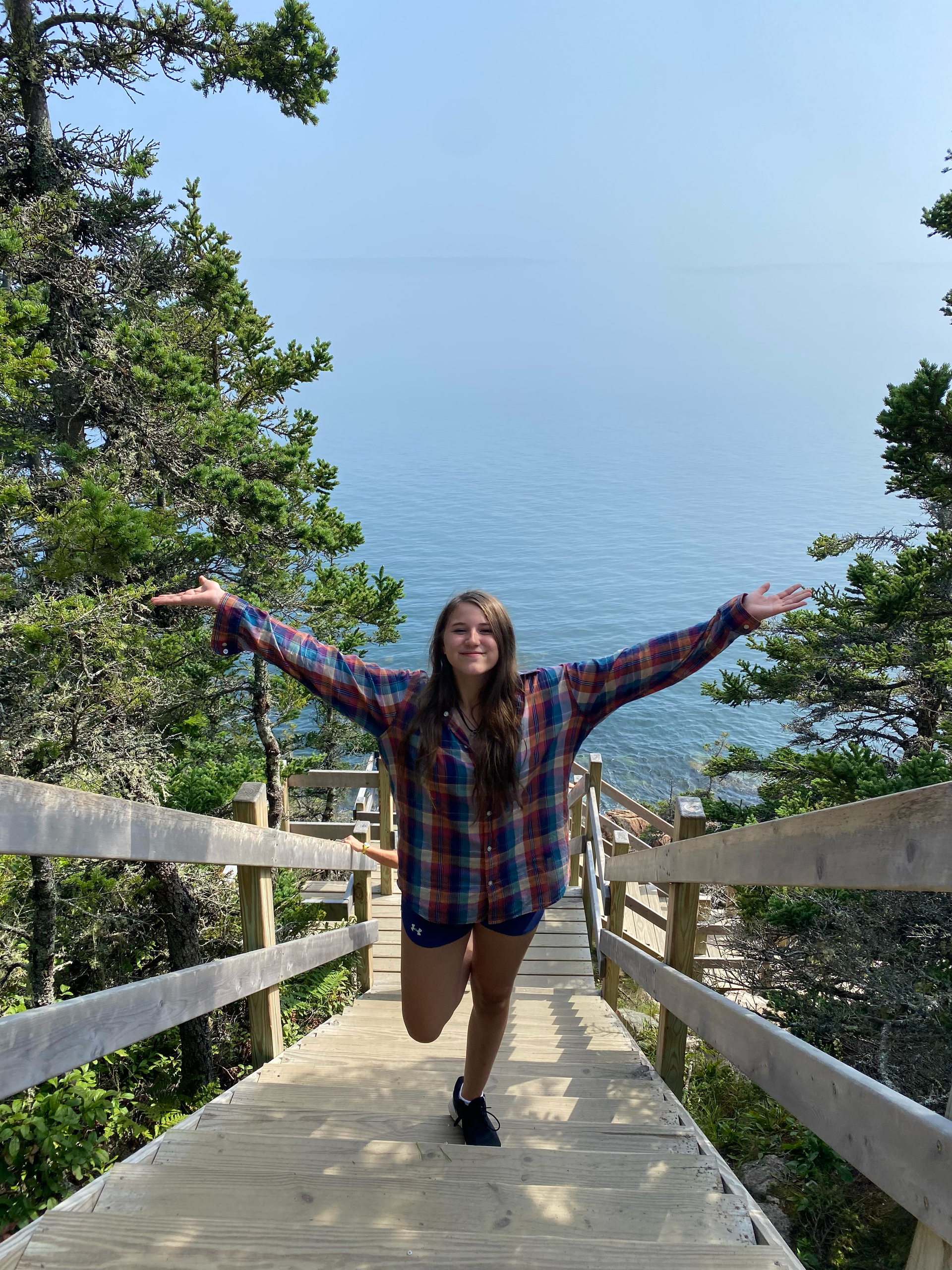 Nathalie is standing on a wooden bridge with her arms outstretched near Bass Harbor Head Light Station.