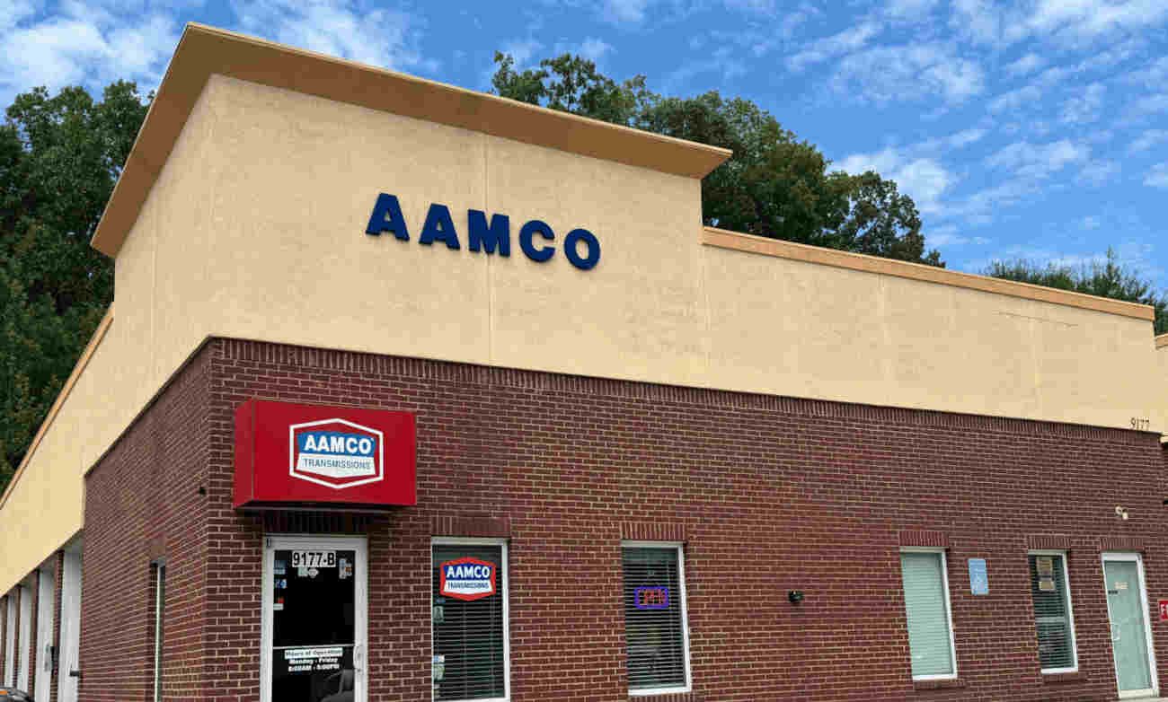 AAMCO mechanic showing a man a tablet while working on a car engine in an AAMCO garage.