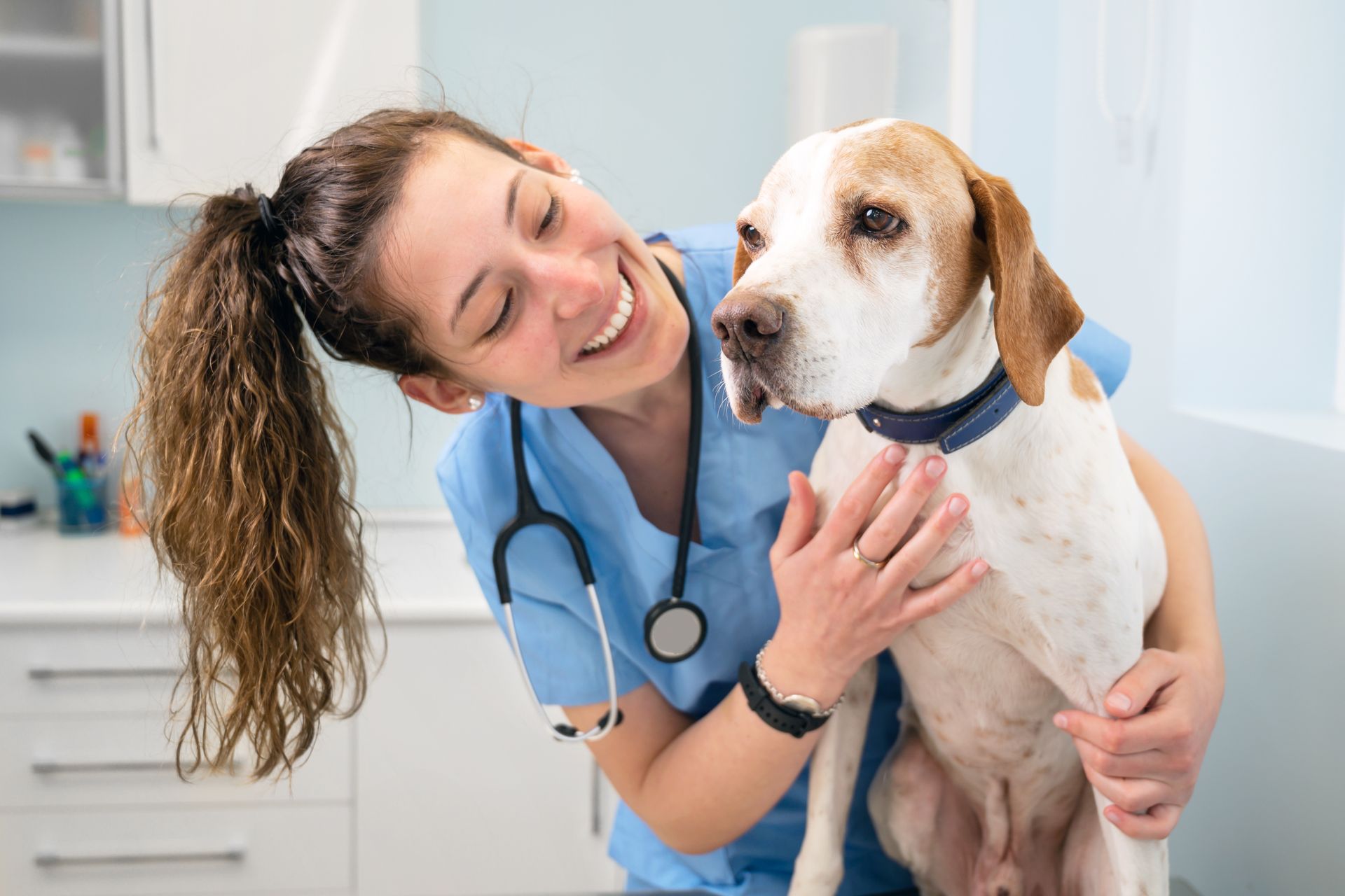 A young, happy female veterinary nurse is smiling while hugging a dog.