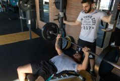 Man bench presses with a spotter at a gym.