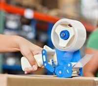 A person is using a tape dispenser to tape a box in a warehouse.