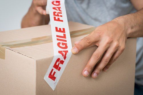 A person is putting fragile tape on a cardboard box.