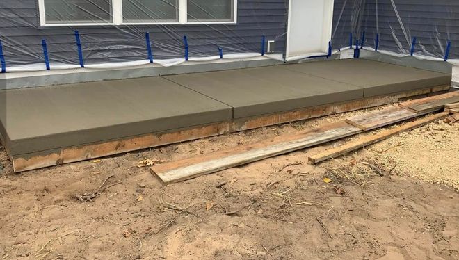 A side view of a house under construction with a patterned stamped concrete patio and Tyvek house wrap on the exterior.