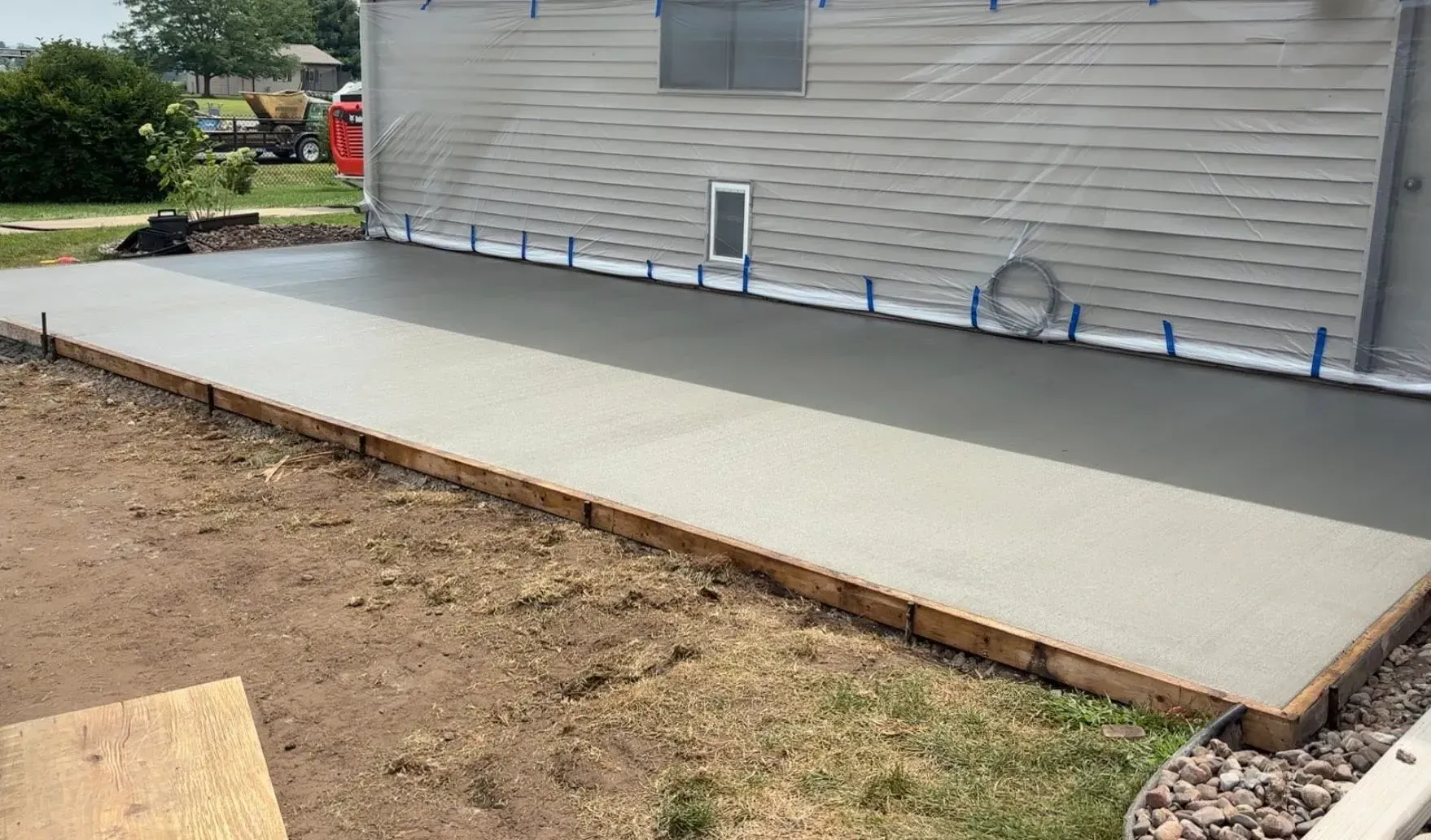 A freshly poured concrete patio framed with wooden boards alongside the gray siding of a house.