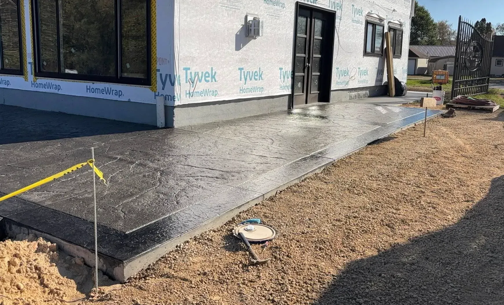 A newly poured concrete patio outside a building under construction, surrounded by a gravel yard.