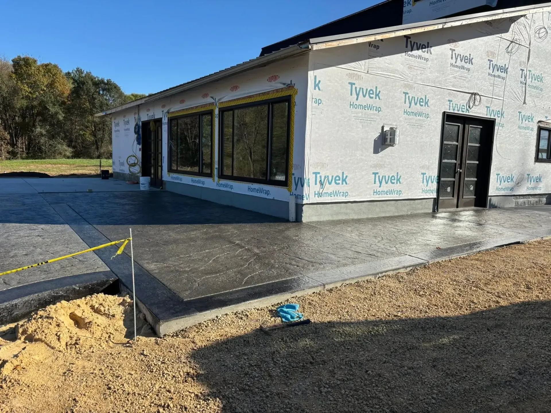 A newly poured stamped concrete patio wraps around the corner of a house under construction with Tyvek house wrap.