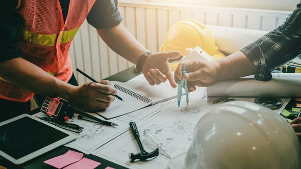 A red construction crane stands above the glass-paneled facade of a building under construction against a cloudy sky.