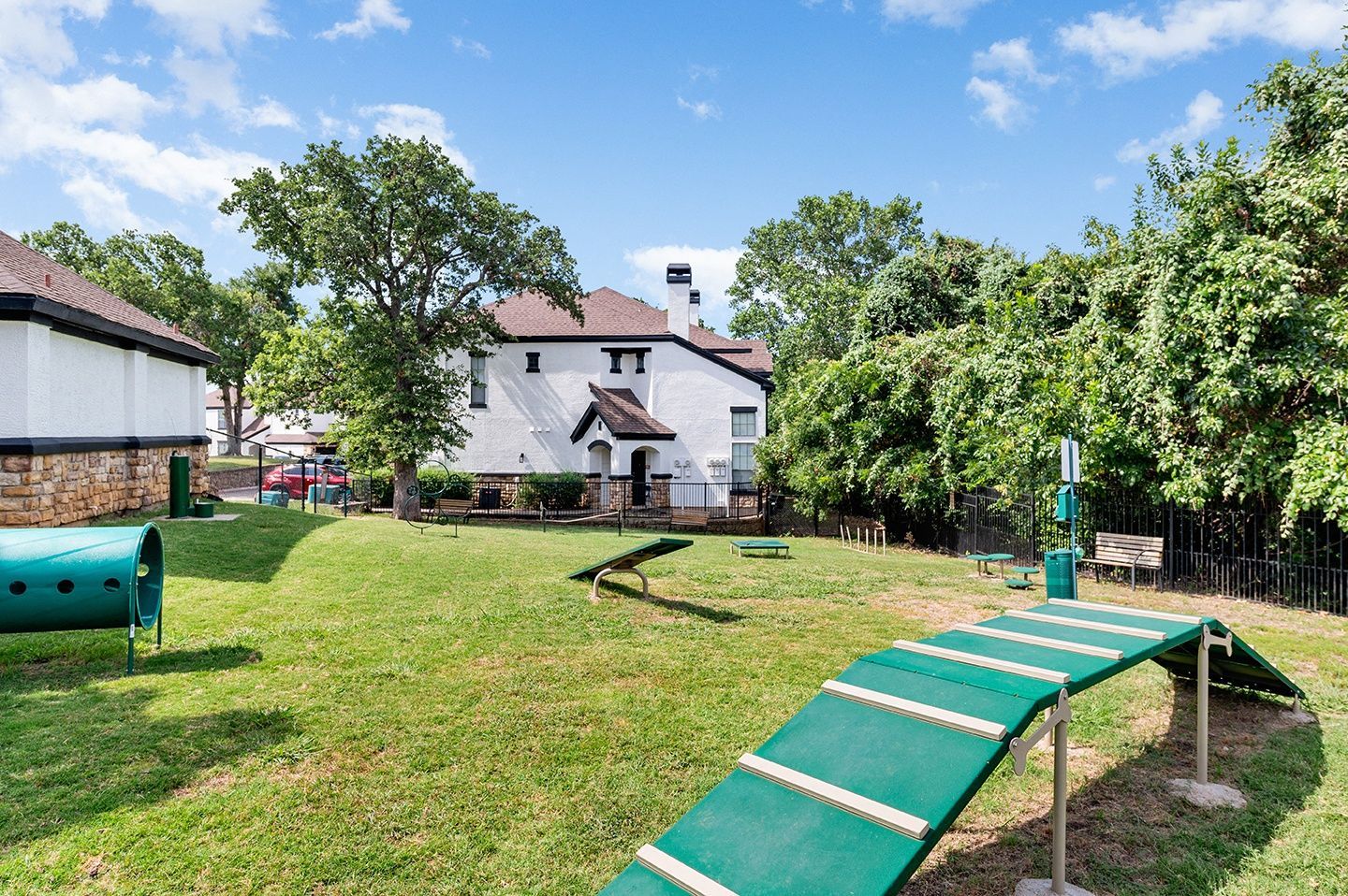 Dog park with green agility equipment on grass, white building in background, sunny day at Villas of Vista Ridge in Lewisville, TX.