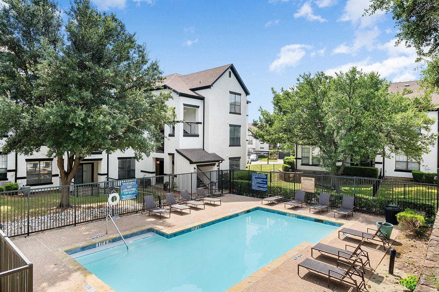 Community pool area with lounge chairs and apartment buildings in the background at Villas of Vista Ridge in Lewisville, TX.