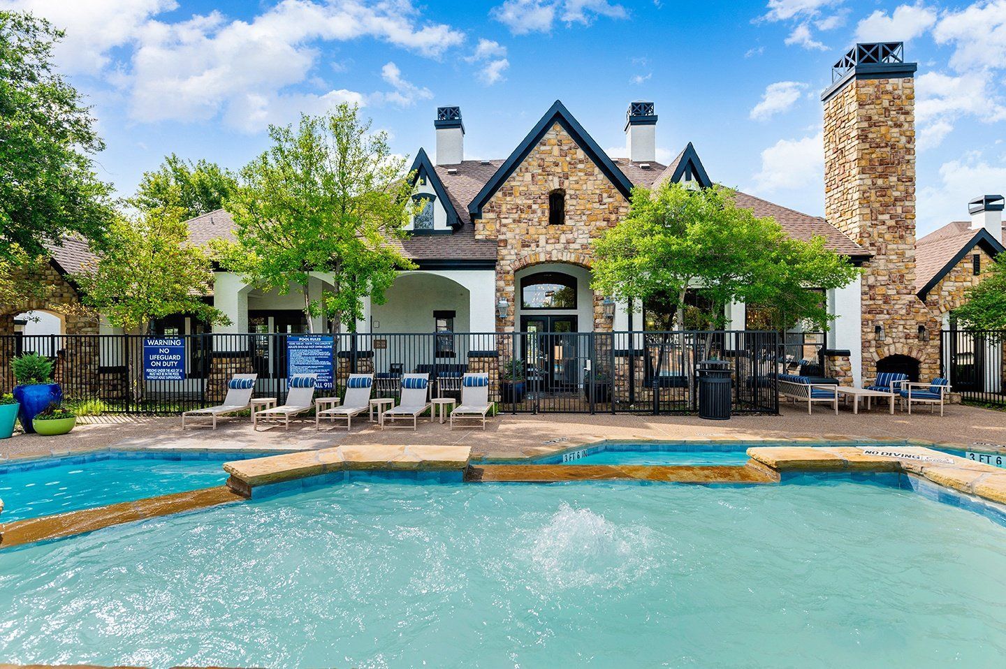 Pool with lounge chairs in front of a stone building with a chimney under a blue sky.