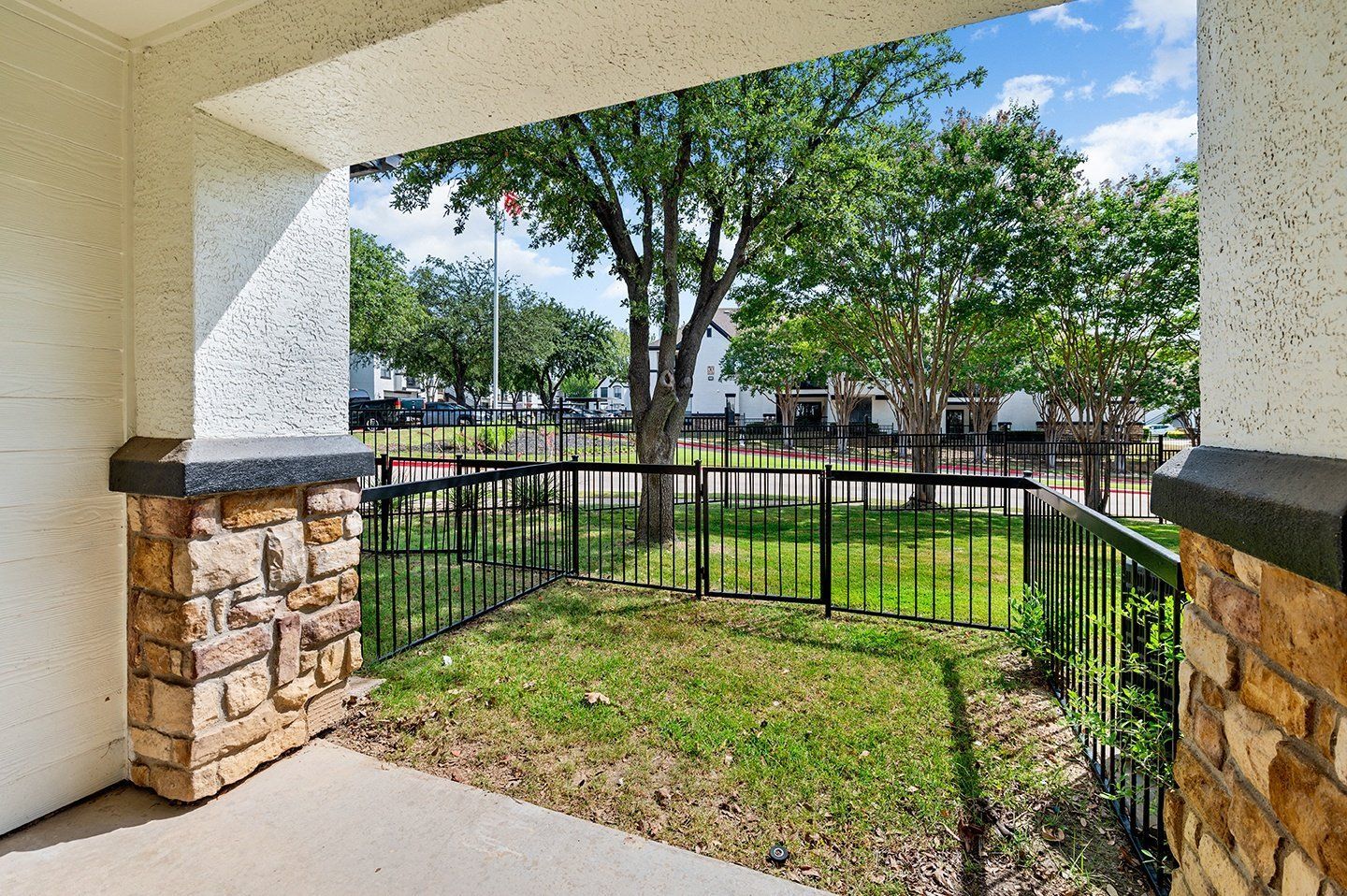 Porch with stone columns, black railing, and view of green lawn and trees.