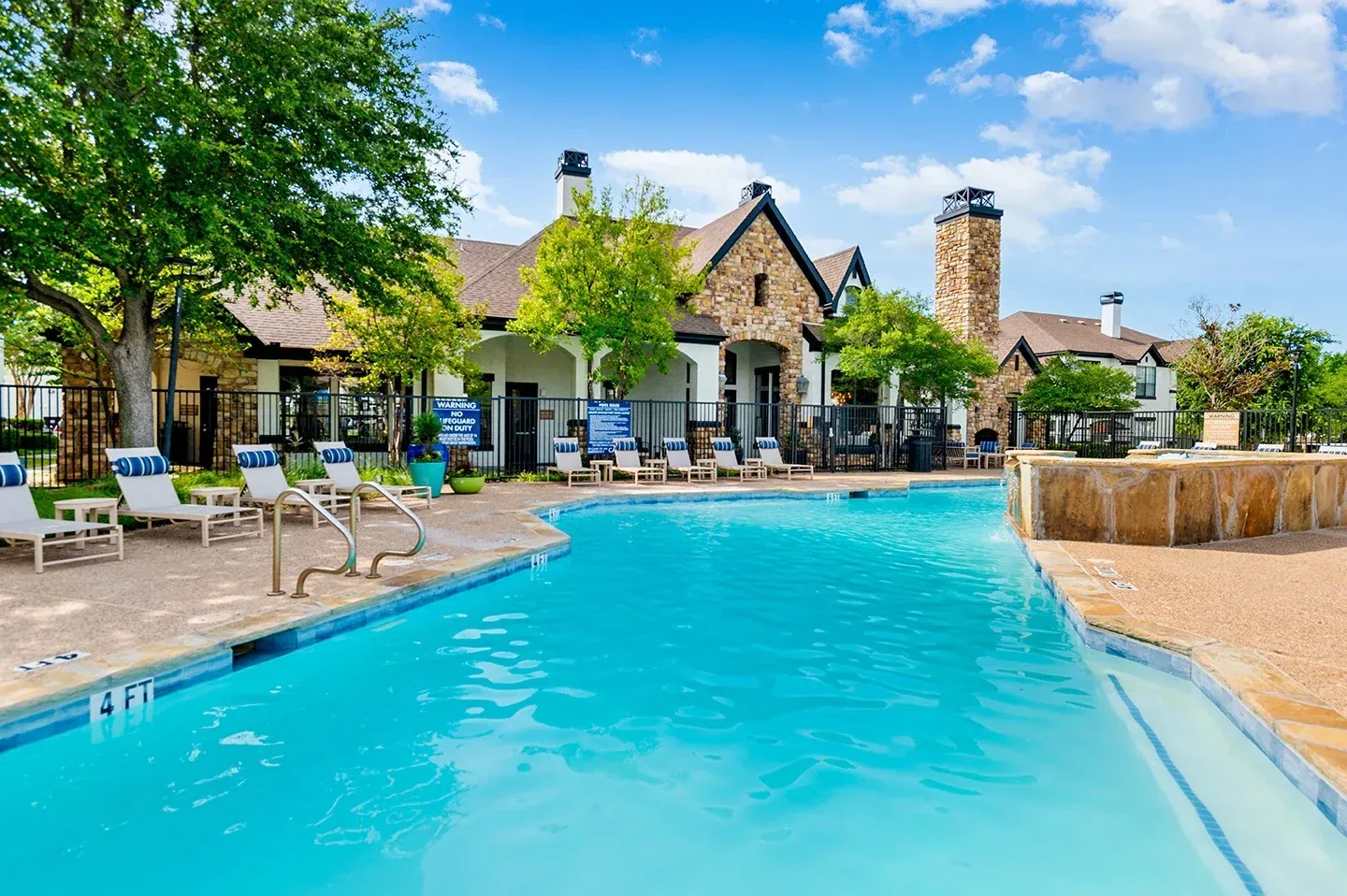 A swimming pool area with lounge chairs and a backdrop of landscaping and building architecture at Villas of Vista Ridge in Lewisville, TX.