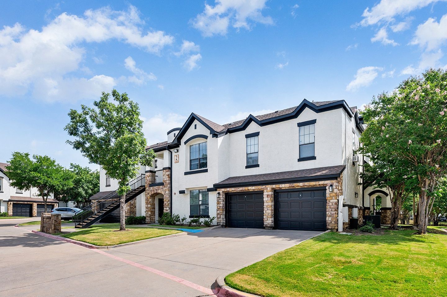 Exterior view of a multi-unit residential building with a driveway and landscaping at Villas of Vista Ridge in Lewisville, TX.